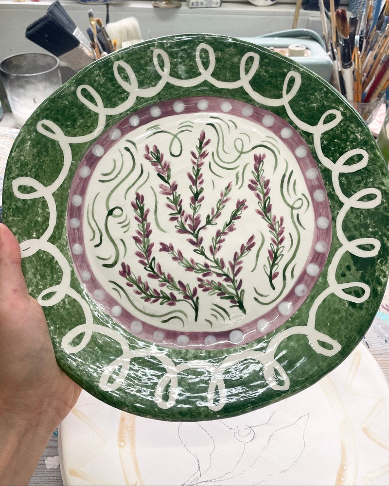 Handmade ceramic plate with floral design held by a person in a pottery studio.