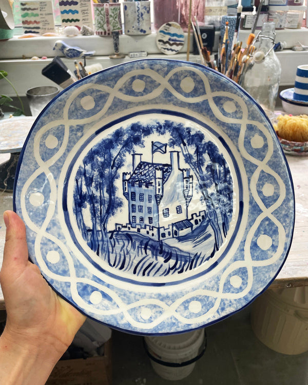 Blue and white ceramic plate with a castle design held by a hand in a pottery studio.