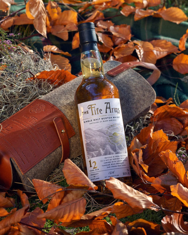 Bottle of The Fife Arms whisky surrounded by autumn leaves and a hat.