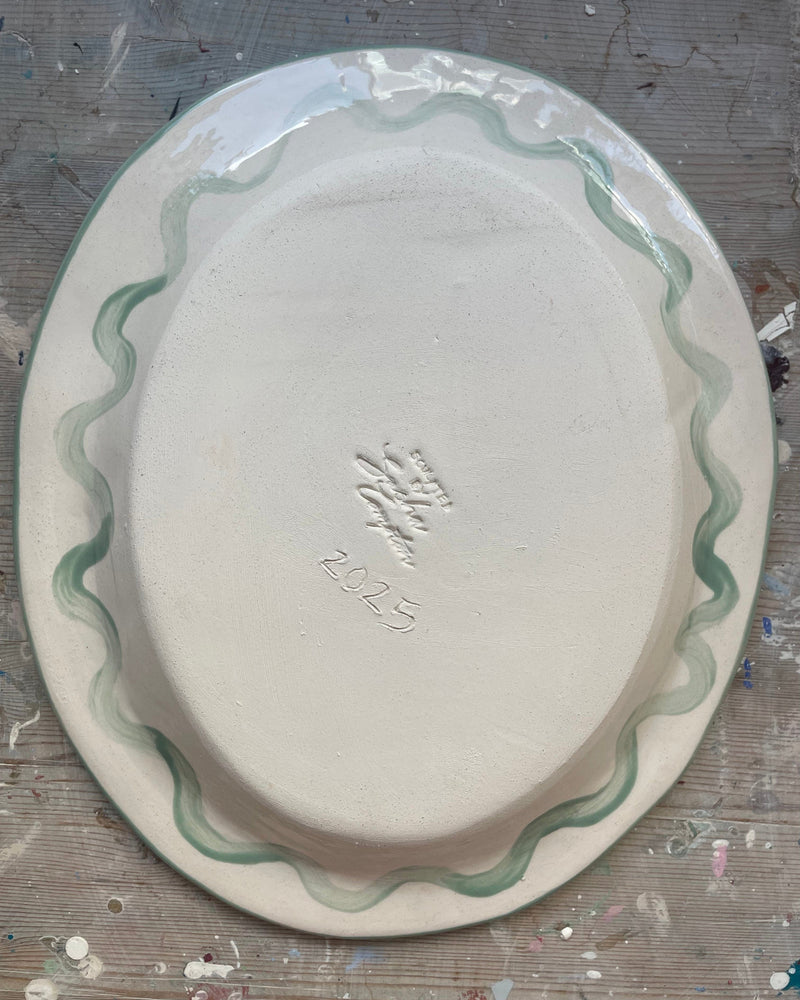 Oval ceramic plate with green decorative edge on a textured surface