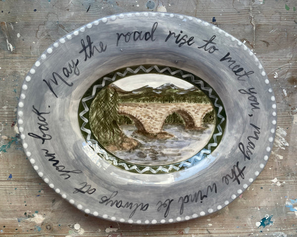Decorative plate with a scenic design and text on a wooden surface