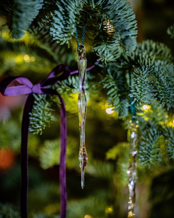 Decorative icicle ornament hanging on a Christmas tree with a purple ribbon.