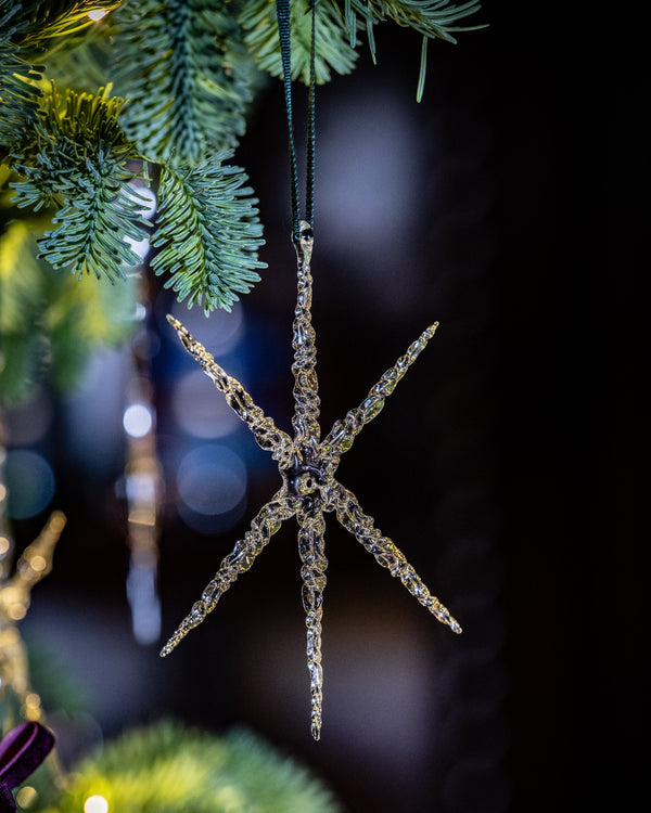 Decorative star-shaped ornament hanging on a Christmas tree with blurred lights in the background.