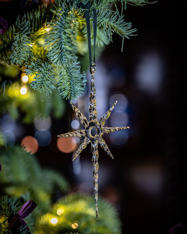 Decorative star ornament hanging on a Christmas tree with blurred lights in the background