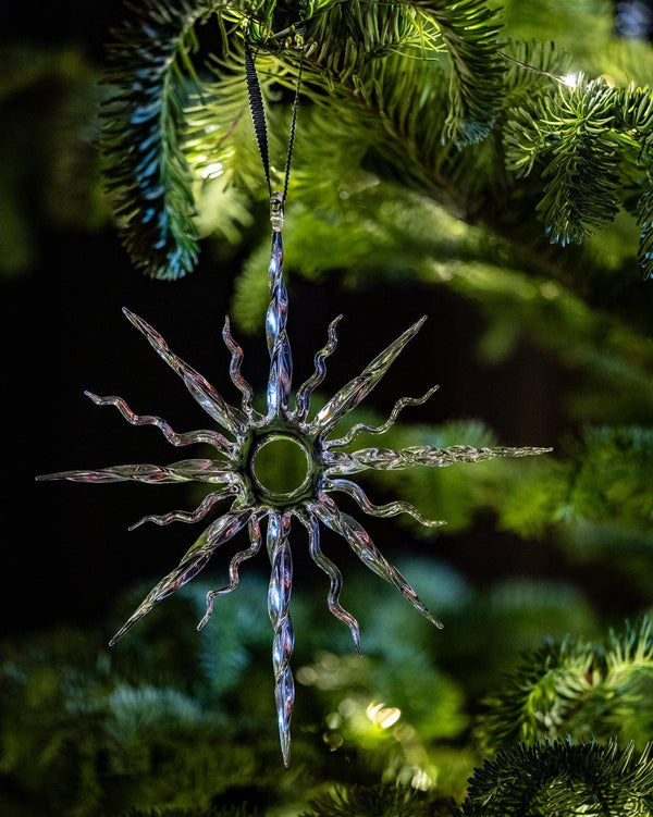Decorative star-shaped ornament on a Christmas tree with green foliage and lights.