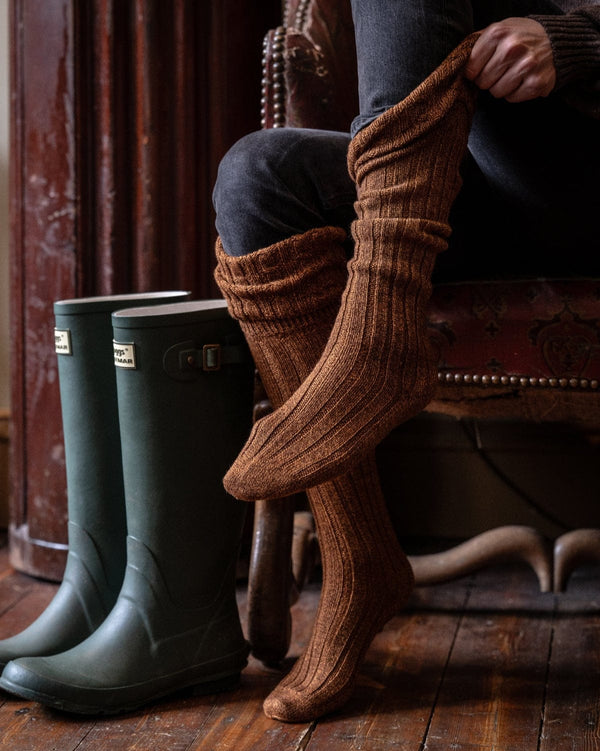 Person wearing brown knee-high socks with green wellington boots on a wooden floor.