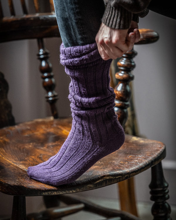 Person wearing purple socks sitting on a wooden chair.