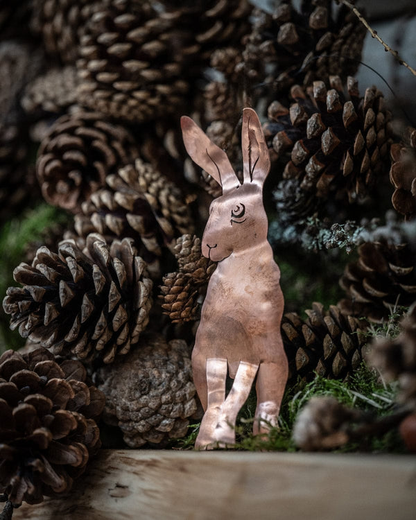 Copper hare figurine among pine cones and moss