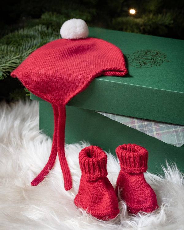 Red baby hat and booties on a green box with Christmas tree in the background