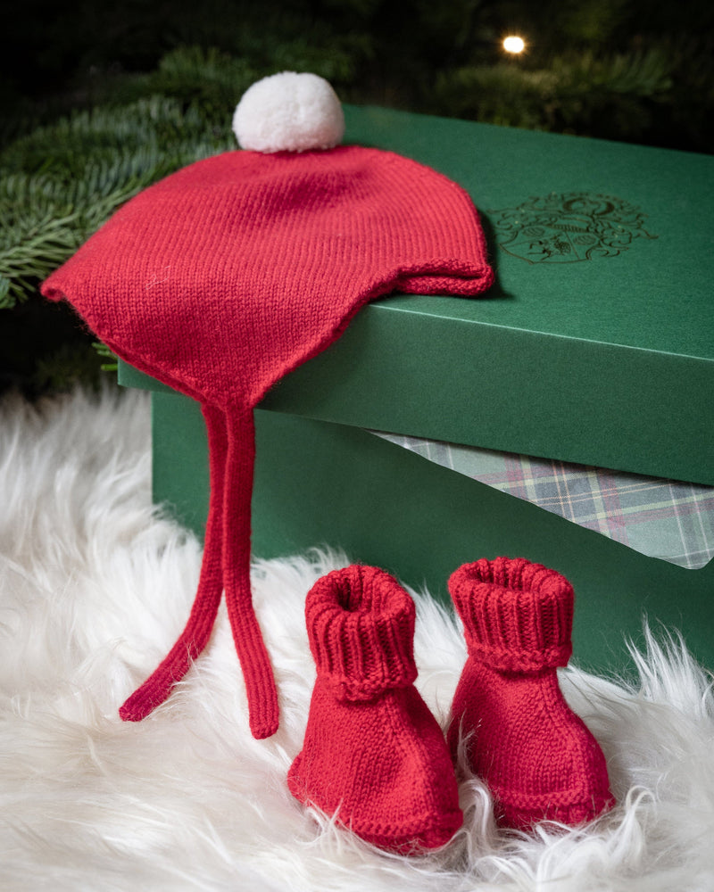 Red baby hat and booties on a green box with Christmas tree in the background