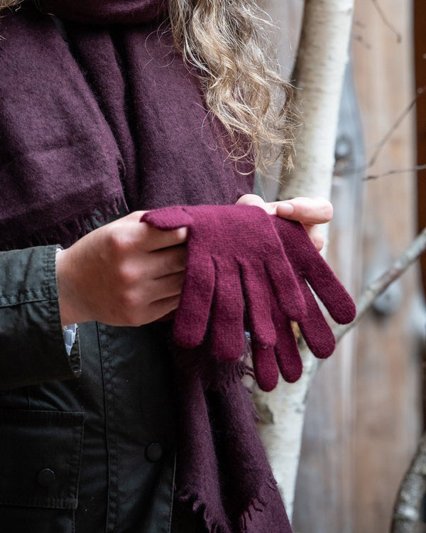 Person wearing a dark coat and holding maroon gloves with a purple scarf.