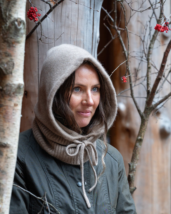 Woman wearing a hooded coat and gloves in a winter setting with bare trees