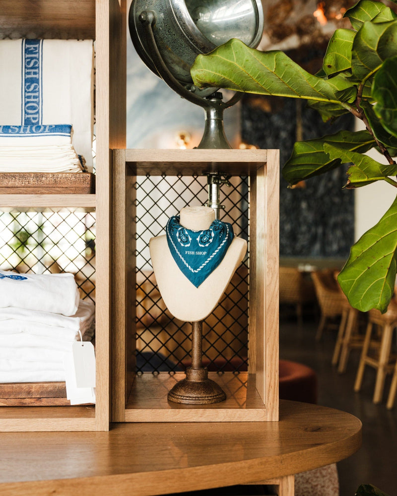 Mannequin head with blue bandana in a wooden frame on a wooden shelf.