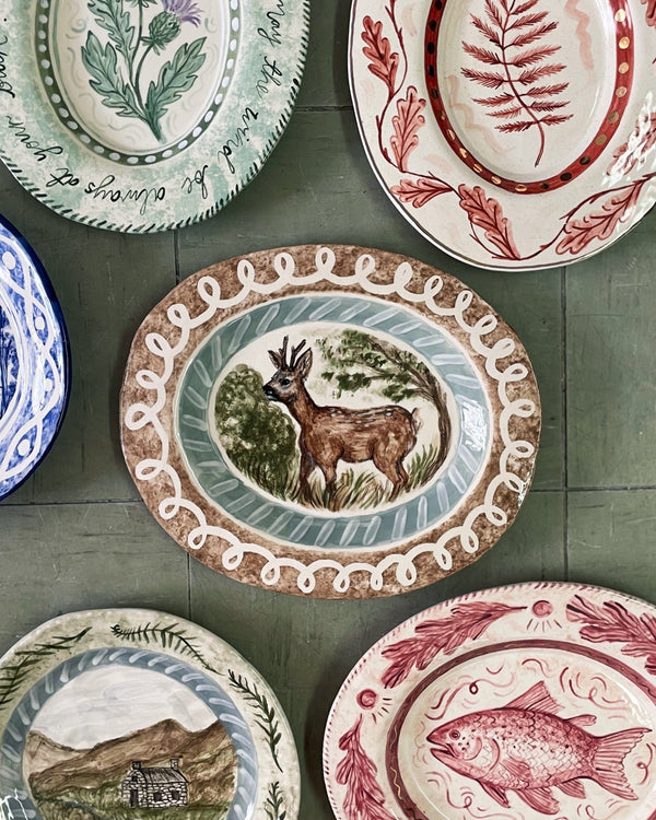 Collection of decorative plates with various designs on a green tiled wall.