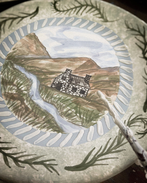 Decorative plate with a painted scene of a house in the mountains