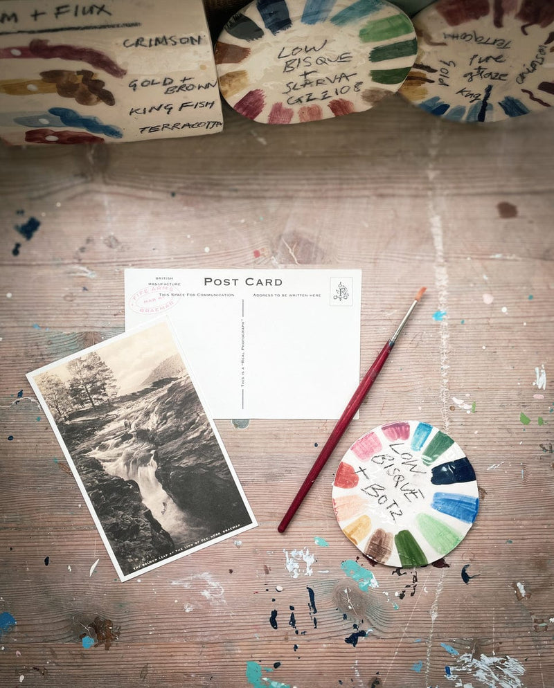 Artistic setup with paint palette, brush, and postcard on a textured surface