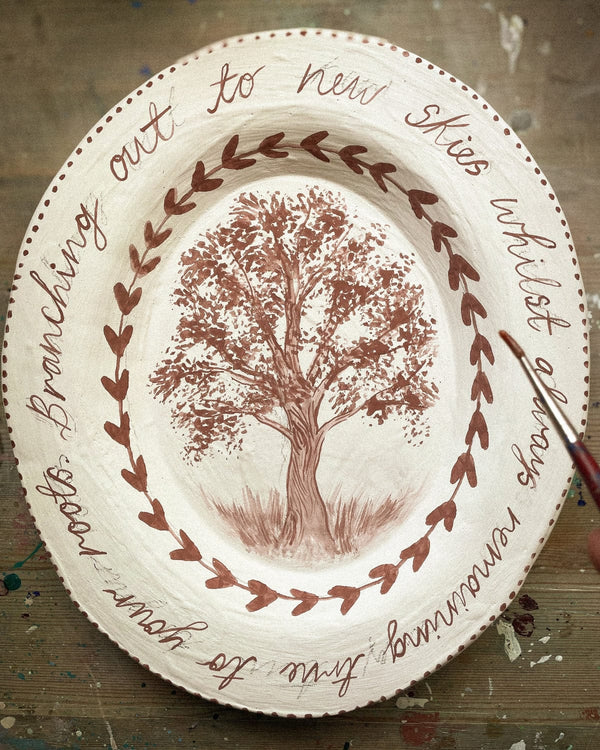 Decorative plate with a tree illustration and text on a wooden surface