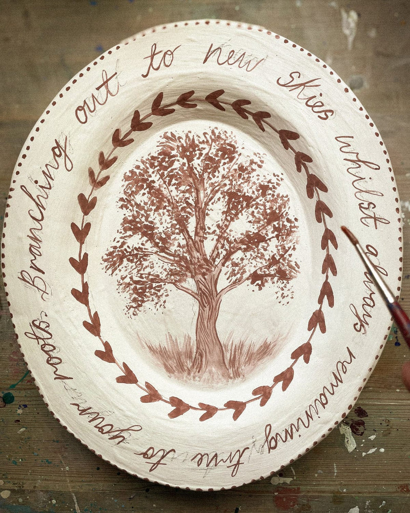 Decorative plate with a tree illustration and text on a wooden surface