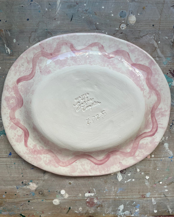 White ceramic plate with pink decorative rim on a textured surface