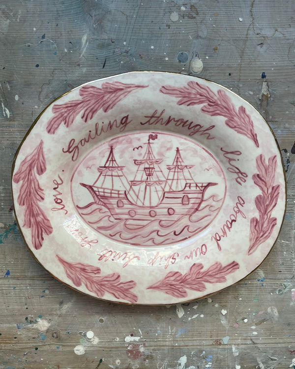 Decorative plate with pink ship design and text on a textured surface