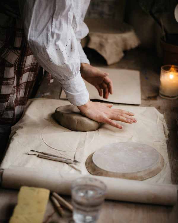 Person working with clay on a table with tools and a candle in the background