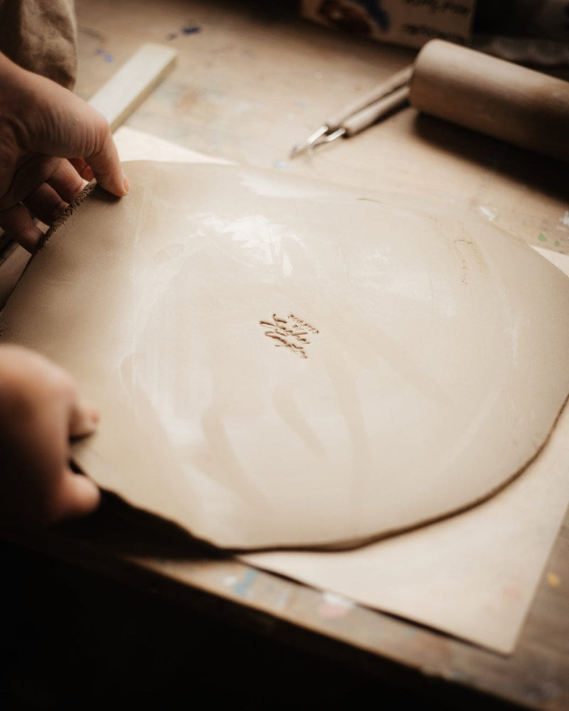 Person holding a large round piece of clay on a pottery wheel