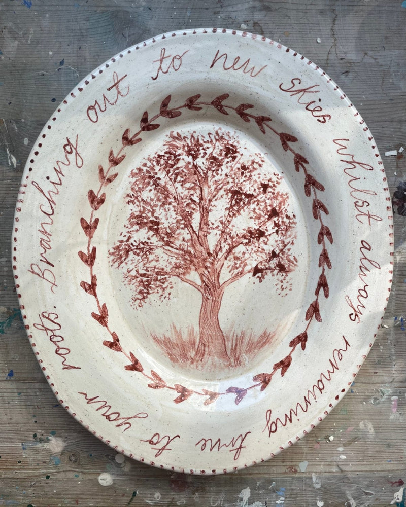 Decorative plate with a tree design and text on a textured surface